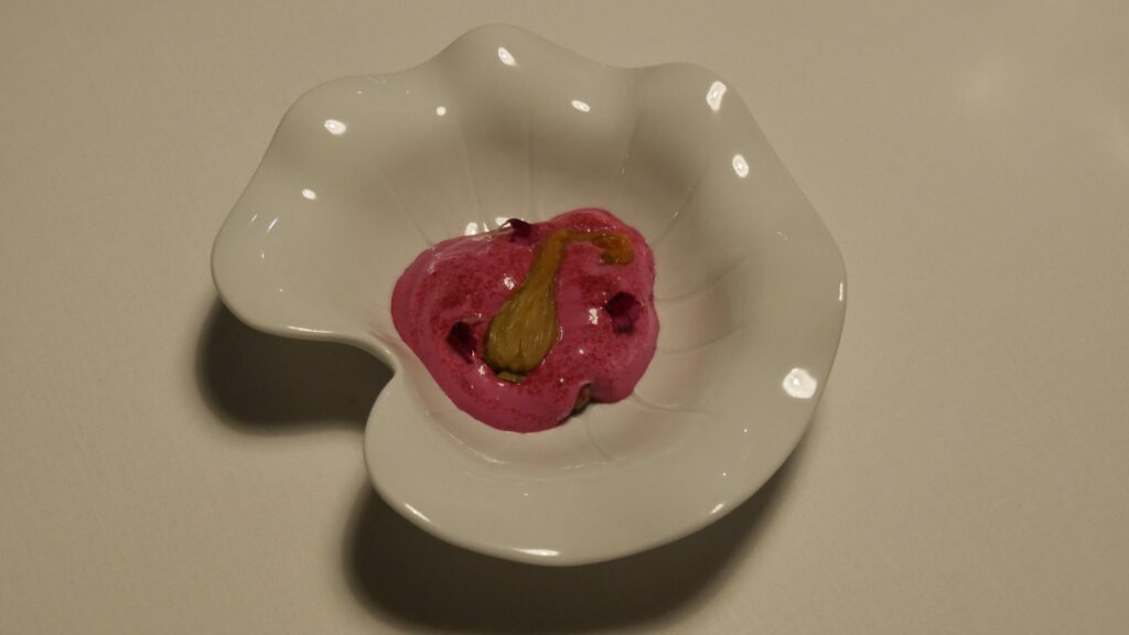 Une assiette en forme de pétale d'orchidée remplie de petites crevettes, d'une mousse rose et d'une courgette.